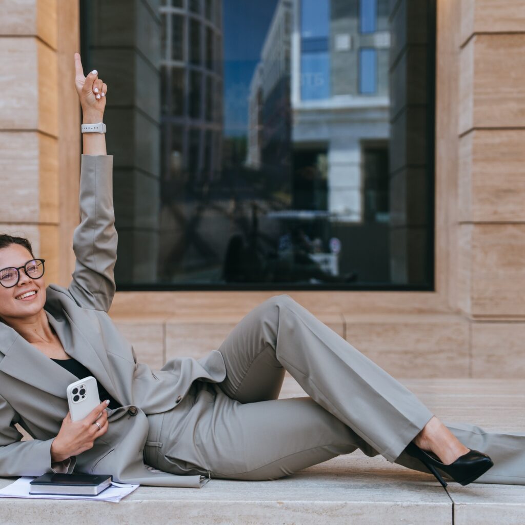 Successful businesswoman in suit laying on building balcony rising finger up celebrating success