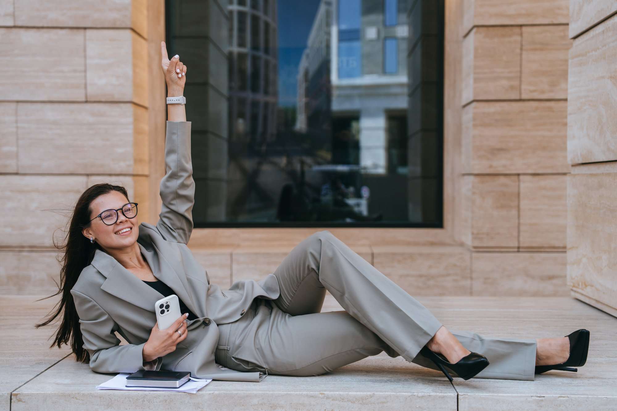 Successful businesswoman in suit laying on building balcony rising finger up celebrating success