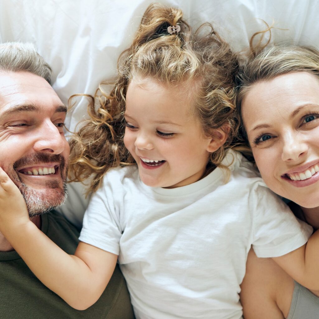 Family, happy and smile of people in bed at home feeling relax in a bedroom bonding. Mother, girl a