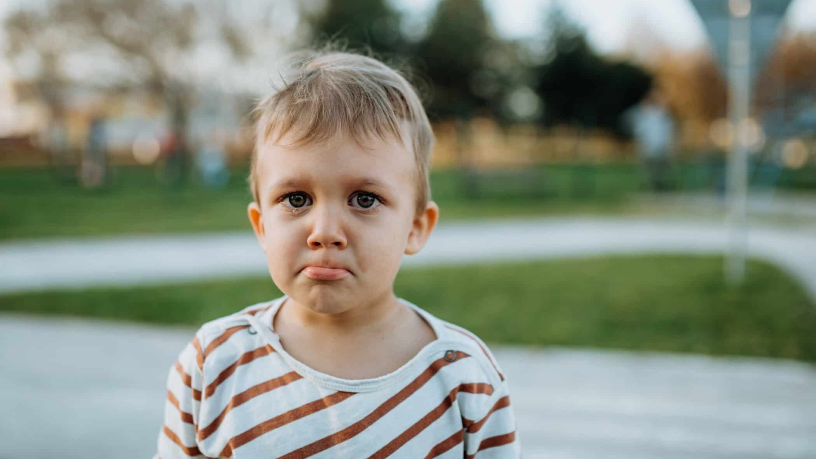 A sad little boy crying outside in park