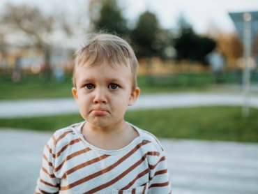 A sad little boy crying outside in park
