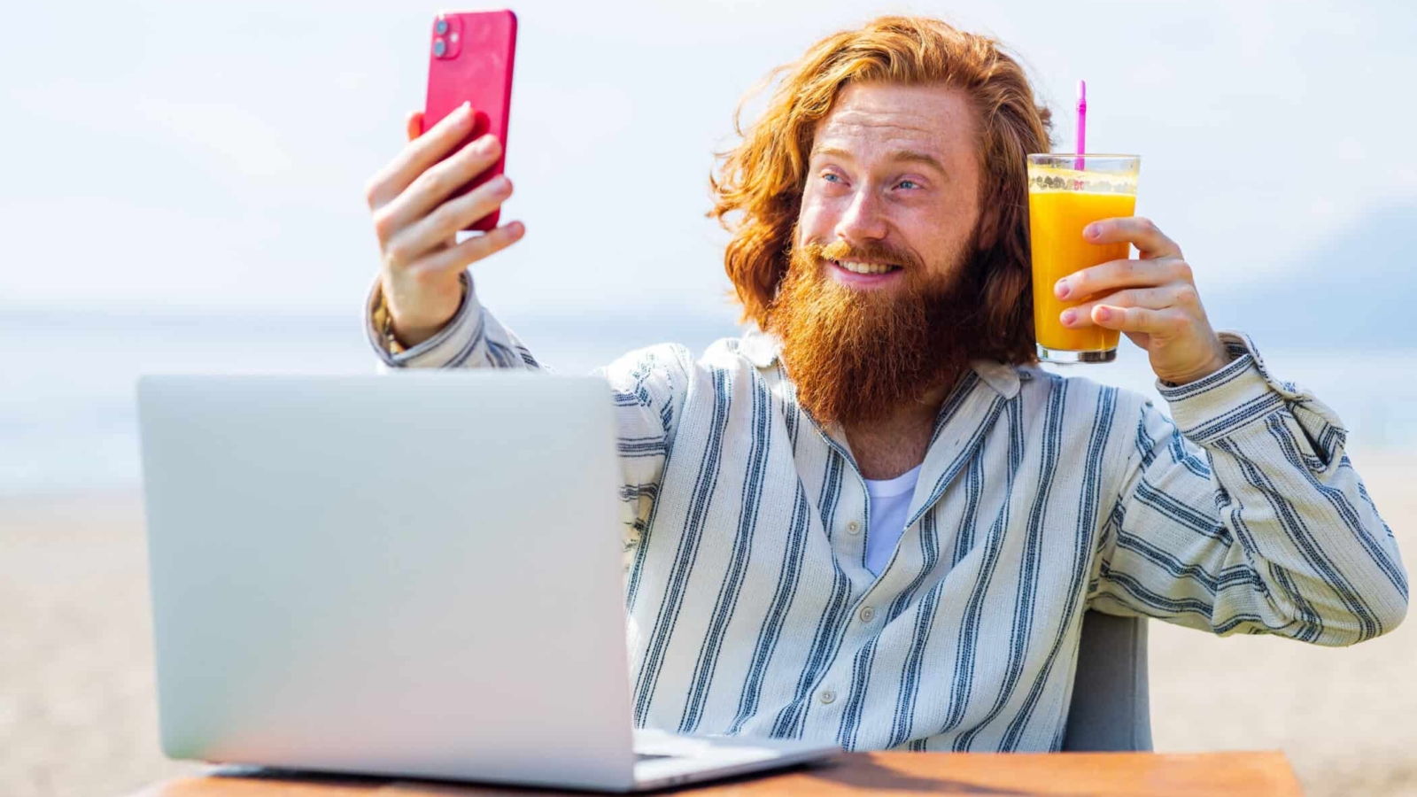 young redhaired ginger bearded man working outdoors in sea cafe with laptop an summer day.